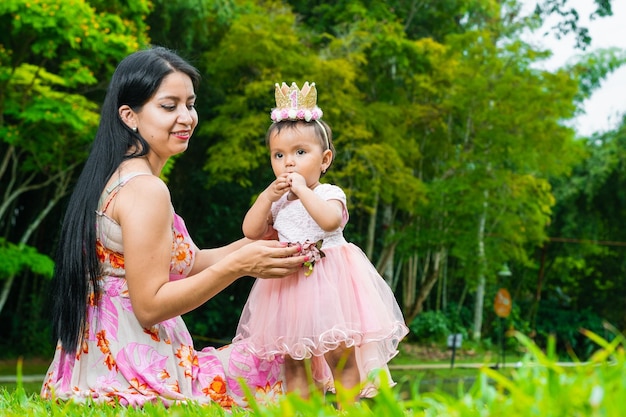 Foto madre latina con la sua bellissima bambina mora seduta mentre la tiene in braccio per non farla cadere madre e figlia in un parco verde