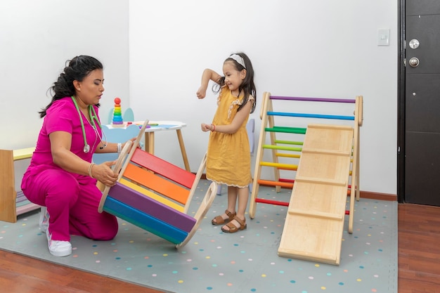 Latina pediatrician doctor checking the motor development of a girl in the play area of her office