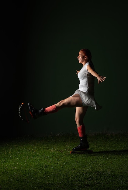 Латиноамериканская рыжая фитнес-женщина в спортивной одежде делает тренировку в ботинках Kangoo Jumps на темно-зеленом фоне