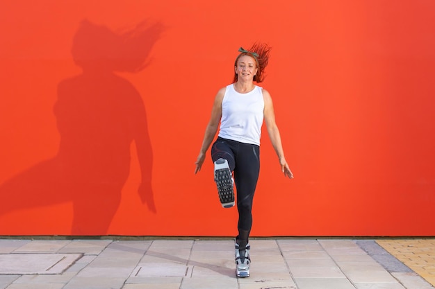 Женщина фитнеса рыжая латина в спортивной одежде делает рутину тренировки, нося ботинки Kangoo Jumps на оранжевом фоне. Активное движение, действие, фитнес и хорошее самочувствие