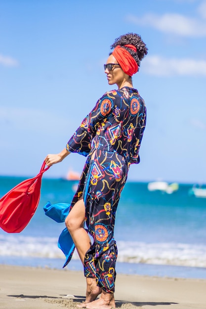 Latina schoonheid slanke vrouw poseren en wandelen met kleurrijke zomerkleding op een tropisch winderig strand