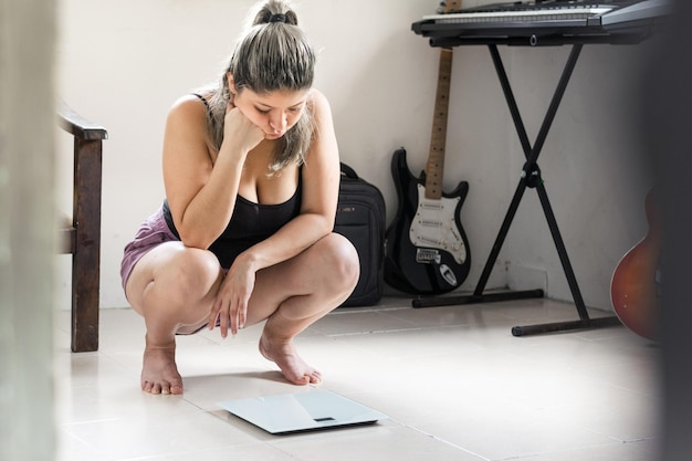 latina vrouw erg verveeld kijkend naar haar gewicht op de weegschaal nadat ze zichzelf had gewogen, meisje bezorgd