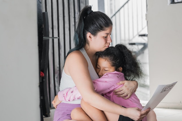 latina vrouw knuffelt haar dochter terwijl ze de brief leest die haar dochter haar cadeau heeft gedaan, teder