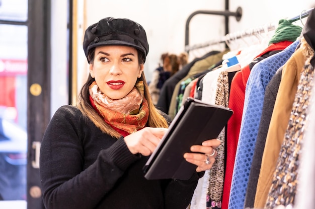 Latina winkelbediende inventariseert met een tablet, tweedehands en duurzame kledingwinkel