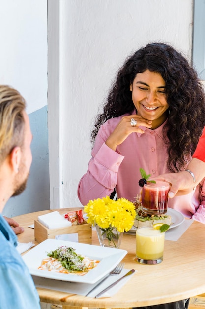 Latina woman eating in a restaurant and smiling. Table with flowers and juice.