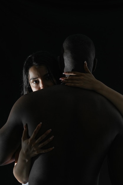 Photo latina woman embracing african american man looking back over her shoulder with black background