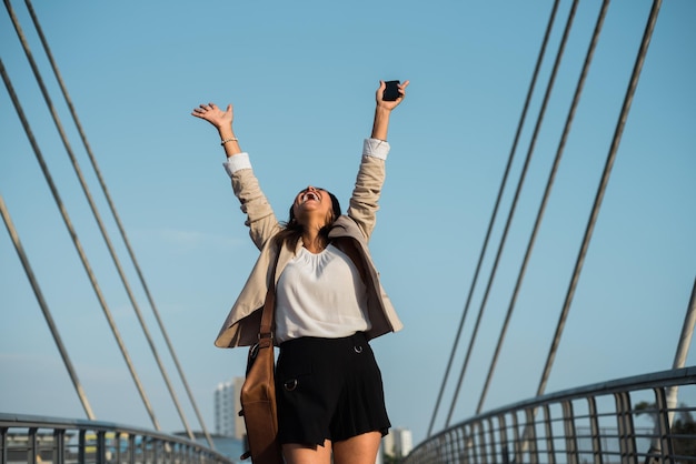 ラティーナの女性が携帯電話で良いニュースを受け取った後、勝利で腕を上げるコピースペース