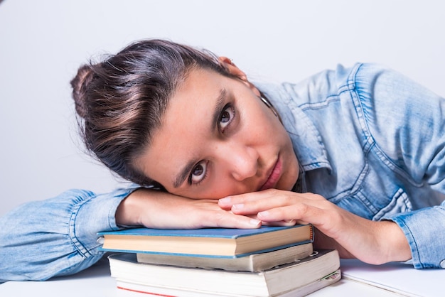 Latina woman studying at home seated close up lying on top of\
her books looking straight ahead college concept