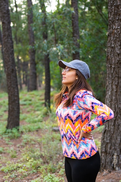 Foto donna latina con berretto multicolore e giacca sportiva che respira rilassata in una foto verticale della foresta