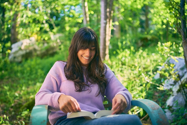 Foto latina giovane donna che legge un libro sorridente è seduta all'aperto