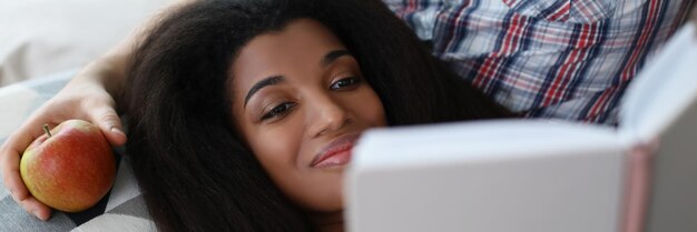 Latino american young woman reading interesting book laying on fathers lap