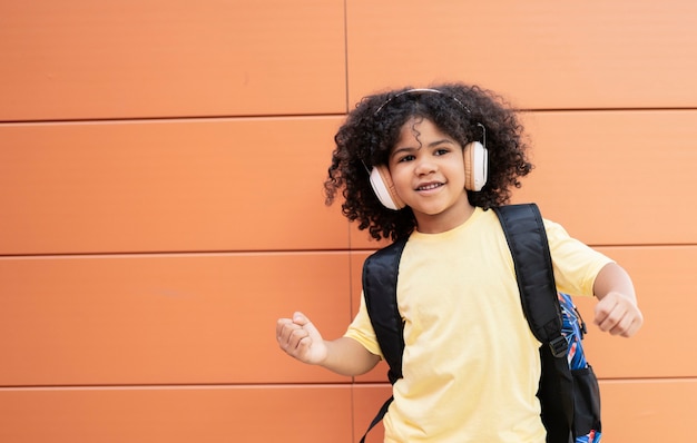 Latino boy wearing headphones and backpack while looking happily at the camera