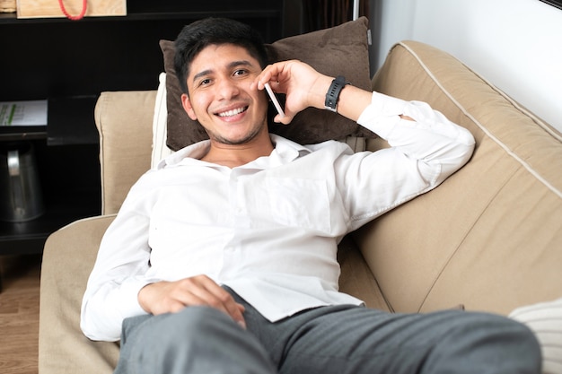 Latino man talking on the mobile phone lying on the sofa at home