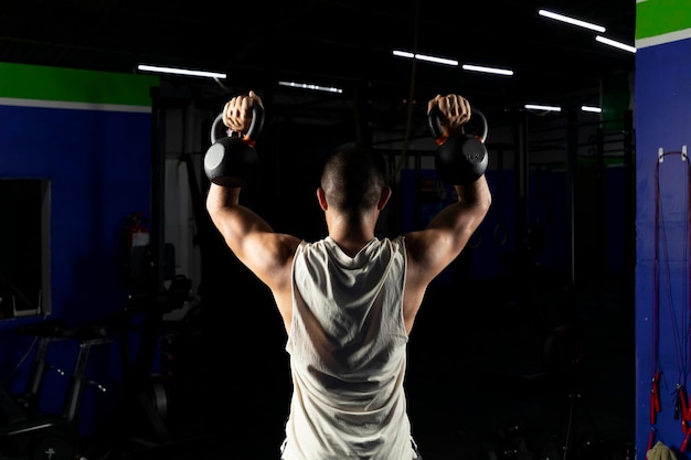 Uomo latino con abbigliamento sportivo che fa stampa con un paio di kettlebell in palestra