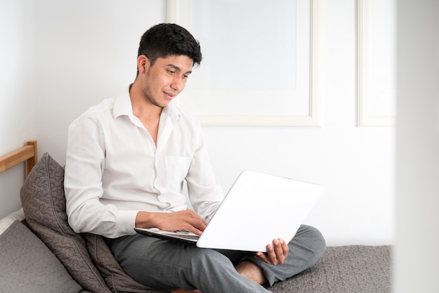 Latino man working in bed with laptop