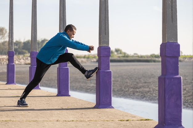 Latino runner stretching against a column of a pergola in a public park with copy space