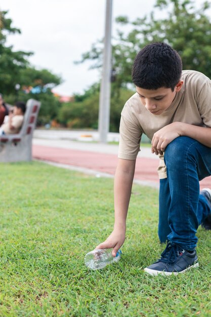 Latino teenager picking up plastic bottle from the ground recycling plastic