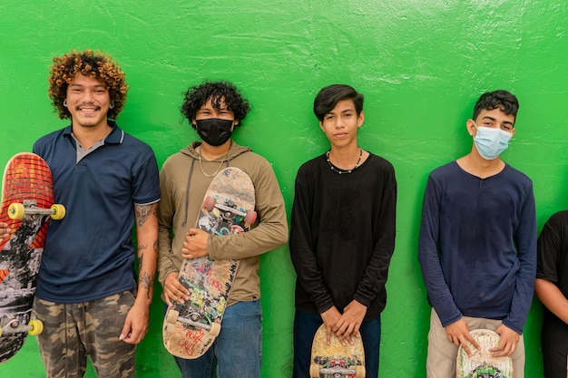 Latino tieners die tegen een muur leunen en lachend naar de camera kijken met hun skateboards