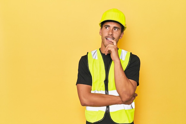 Latino-werknemer in geel vest en helm dacht ontspannen na over iets dat naar een kopieerruimte keek