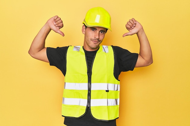 Foto latino-werknemer in geel vest en helm voelt zich trots en zelfverzekerd als voorbeeld om te volgen