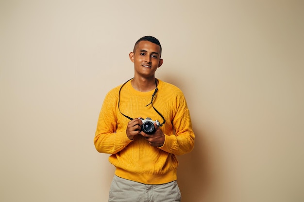 Latinx man wearing a yellow sweater holding with the hands an vintage camera