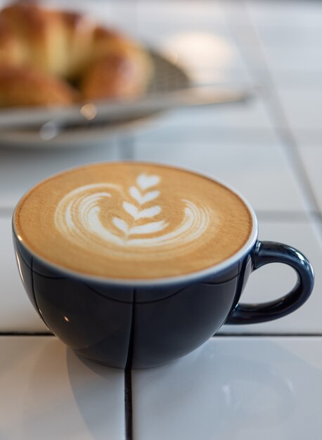 Tazza e croissant di caffè di arte del latte sulla tavola bianca