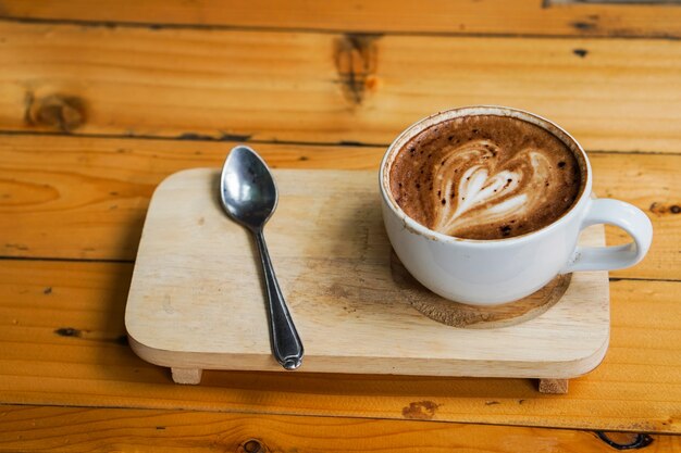 Latte art coffee heart picture placed on wooden tray, on the wooden table background.