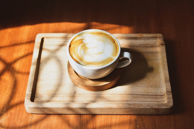 Latte art coffee on wooden table sunlight at window