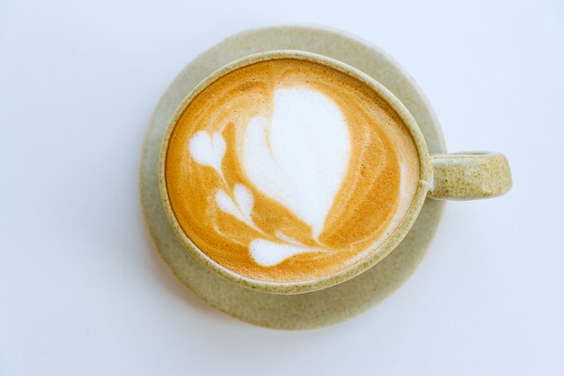 Latte art in cup on white backdrop, top view