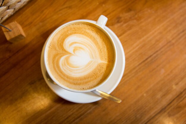 latte art, drink , love and object concept - close up of coffee cup with heart shape drawing on cream froth