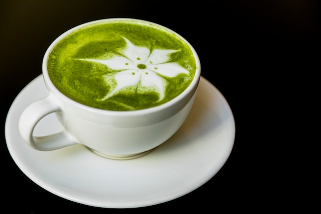 Latte bloemkunst met Japanse groene theematcha in kop op zwarte achtergrond