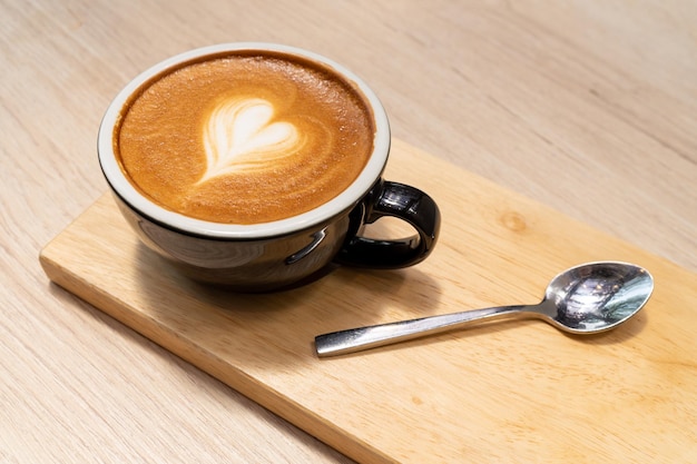 Caffè latte o cappuccino in tazza nera con bella arte del latte del cuore sulla tavola di legno