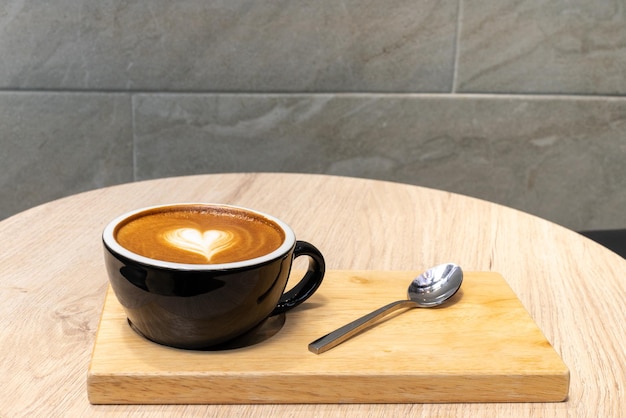 Latte coffee or cappuccino coffee in black cup with beautiful heart latte art on wooden table