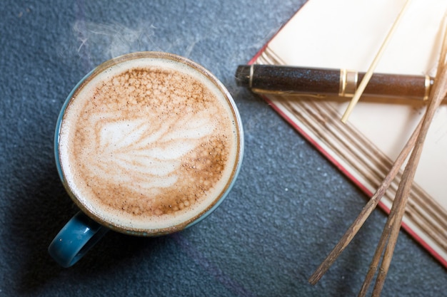 Кофейная чашка Latte, ручка, книга и высушенные цветки на деревянном.
