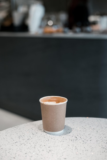 Latte coffee on a paper cup served on white table at cafe