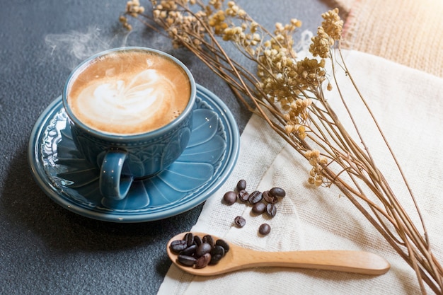 Чашка латте, кофейное зерно и высушенные цветки раздражают на деревянном.