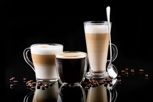 latte macchiatos in a glass cup with handle with coffee around and spoon isolated on dark background