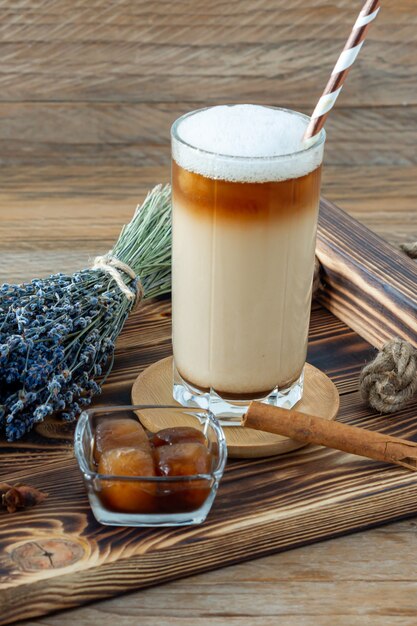 Latte of cappuccino met melkschuim en lavendel in een hoog glas op houten dienblad.