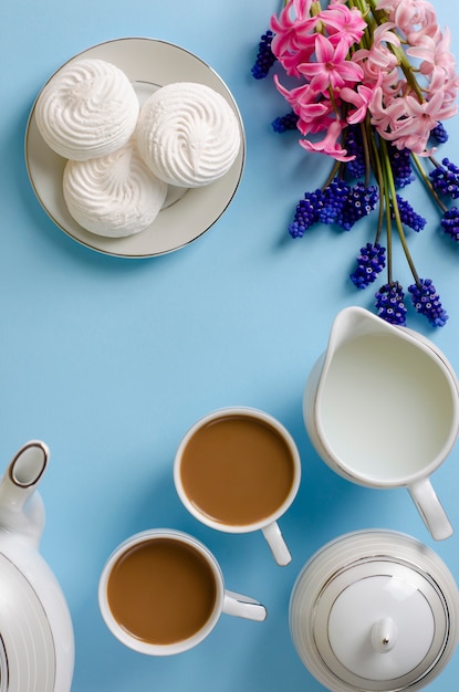 Latte, witte schuimgebakjes, melkkruik op pastelkleur blauwe die achtergrond met muscari en hyacintbloemen wordt verfraaid.