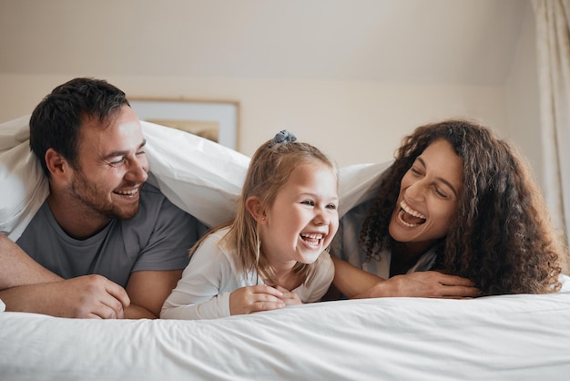 Photo laugh happy and family in bed together bonding with comic comedy or funny joke together smile love and young girl child relaxing and having fun with her mother and father in the bedroom at home