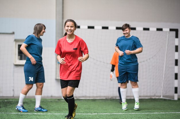 Laughing active girl in sports uniform running down green football field