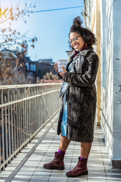 Laughing active woman. Cheerful young lady holding strapped cup and warming up in sun lights