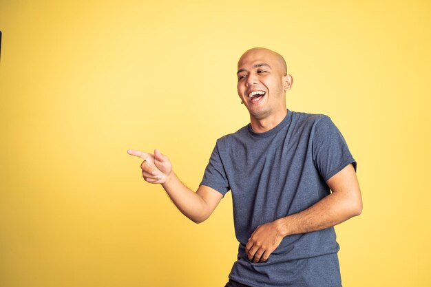 Laughing asian bald man with finger pointing on isolated background
