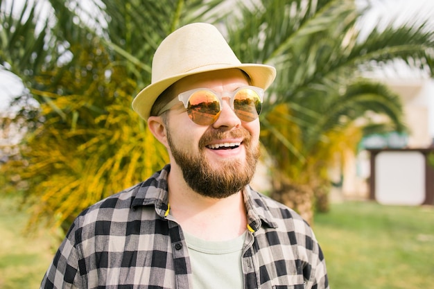 Смеющийся привлекательный мужчина в шляпе на фоне пальмы, эмоции и концепция отпуска, путешествия, праздники