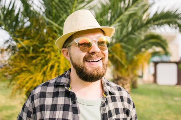 Laughing attractive man wearing hat over palm tree background emotion and vacation travel holidays concept