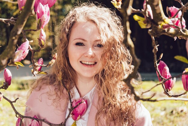 Laughing attractive woman posing in a park next to a fragrant blooming magnolia