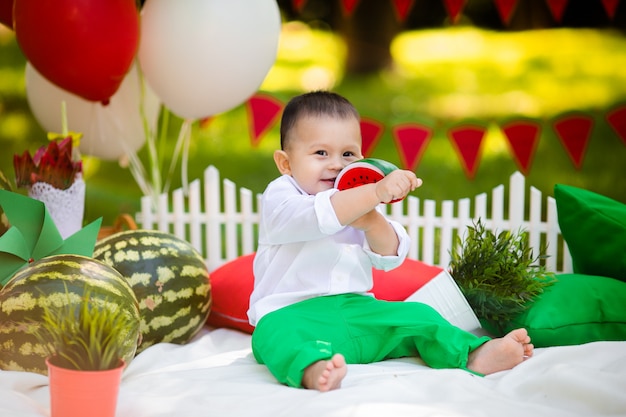 Laughing baby boy 1-2 year old eating watermelon outdoors. Summer party concept