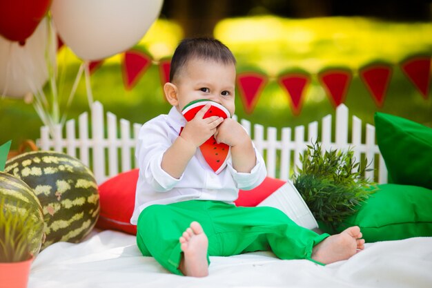 1〜2歳の男の子が屋外でスイカを食べて笑っています。夏のパーティーのコンセプト