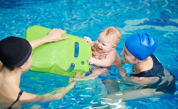 Laughing baby enjoying his first swimming in pool Little infant playing with floating board Active lifestyle for child