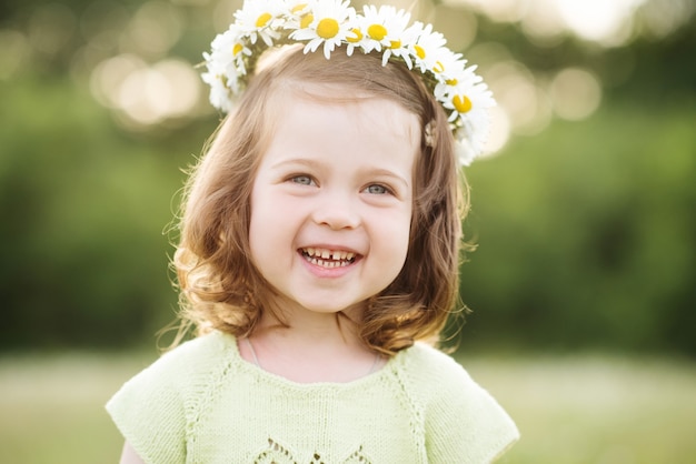 Laughing baby girl with blonde hair wearing chamomile flower wreath